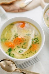 bowl of chicken soup with spoons on the side parsley garnish