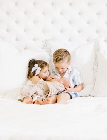 brother and sister cuddling baby brother in bed