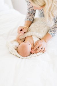 mom wrapping newborn in cream knitted blanket