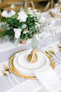 Pear with a paper leaf name tag on white gold-trim plates with white flower centrepiece on a table as party decor