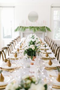 long party table decor with golden pears on gold trimmed white plates and glasses with white flower centrepieces
