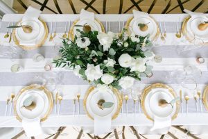 Top view of golden pears on top of gold trimmed white plates with matching utensils and glasses and white flower