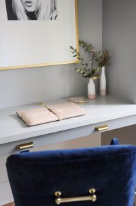 grey desk with gold handles and laptop in a pink case with two vases of flowers