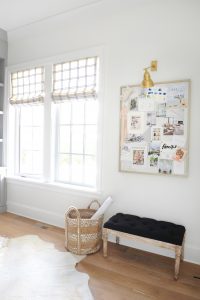 two windows with drapes next to an inspiration board with a basket and a seating bench