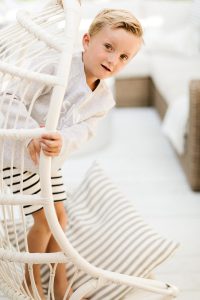 young boy standing on a swing chair wearing sun kissed crew neck sweater
