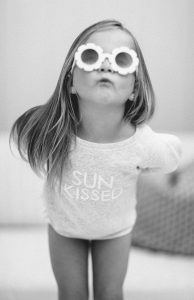 Young Girl wearing sun kissed crew neck sweater and daisy sunglasses blowing kisses