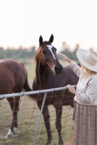 blonde woman wearing country girl sweater petting a horse