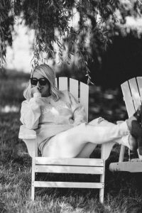 blonde woman wear sunglasses sitting on lawn chairs with legs propped up wearing sun kissed crew neck sweaters