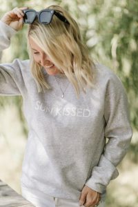 blonde woman wearing sunglasses and sun kissed crew neck sweater