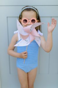 little girl wearing sunglasses and a bathing suit holding a pinwheel