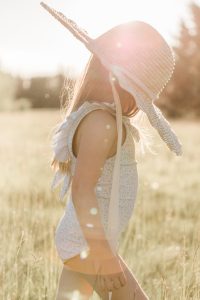 little girl wearing straw hat and swimsuit walking through grass